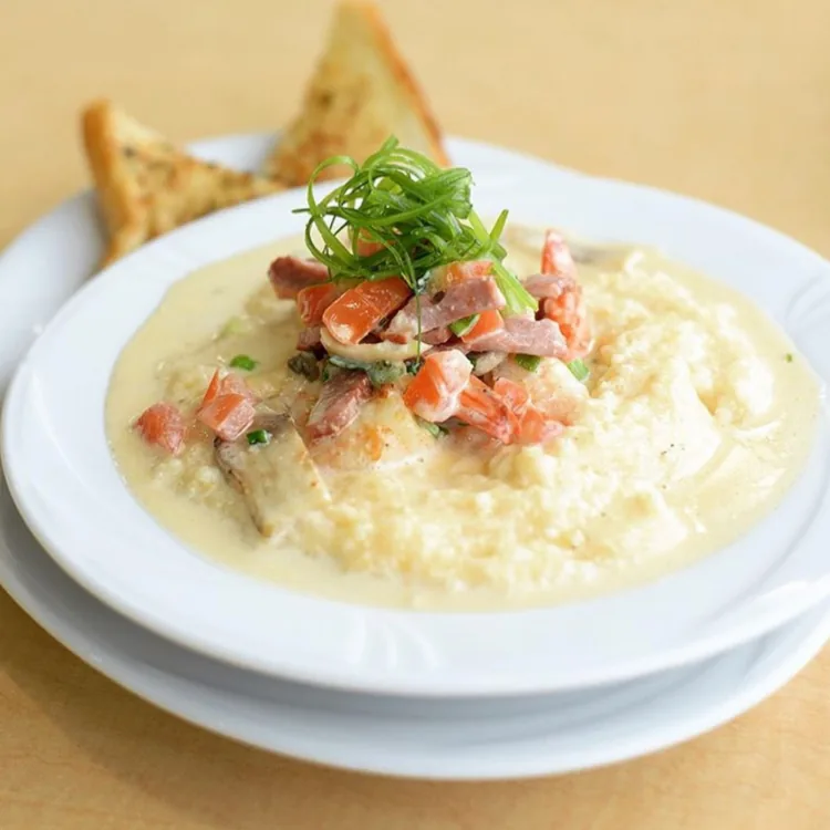 Shrimp and grits in a white bowl with scallions and a wedge of garlic Texas toast